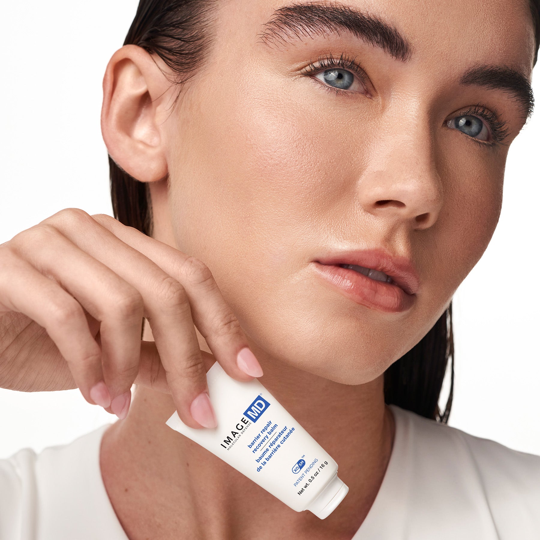 Woman holding a skincare product with a close-up of her face.