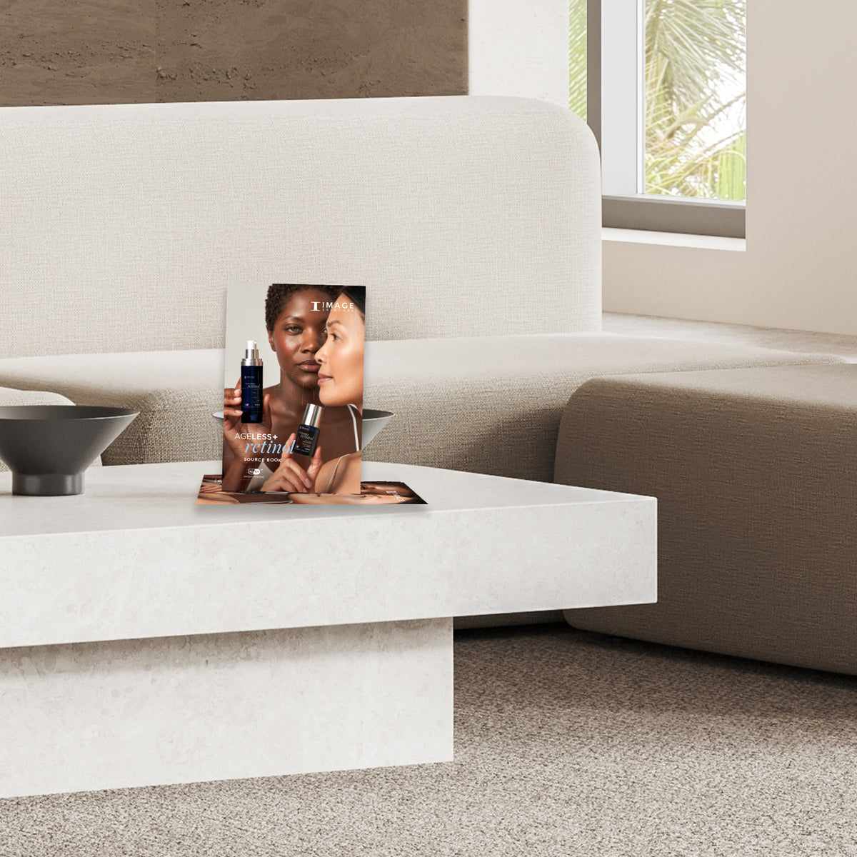A book titled 'AGELESS+ retinol Source Book' displayed on a modern white coffee table with a contemporary interior background.